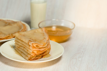 Maslenitsa is a holiday at the end of February . pancakes with honey and milk on a light background. honey trickles down a stack of pancakes. close up. blini. space for text