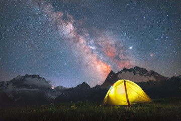 tourist yellow tent in a meadow against the background of mountain peaks and the Milky Way in the...