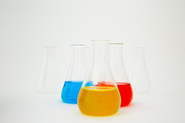 Scientific laboratory glass erlenmeyer flask filled with blue, yellow and red liquid on white background.