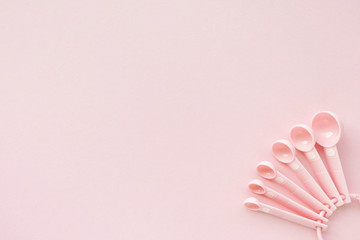 Measuring plastic spoon in pink color on pink background, top view, copy space