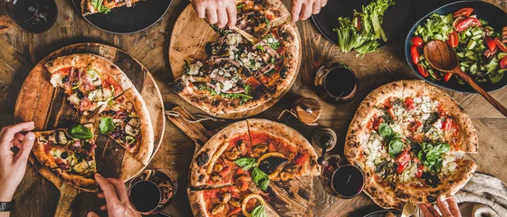 Foto op Plexiglas Family or friends having pizza party dinner. Flat-lay of people eating various kinds of Italian pizza and drinking wine over wooden table, top view, wide composition. Fast food lunch concept © sonyakamoz