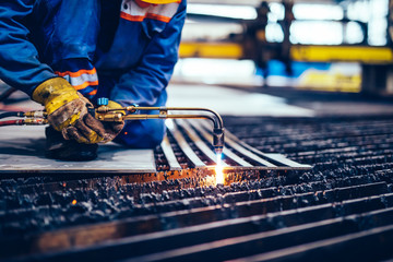 Worker cutting metal, steel with acetylene torch in big factory.