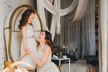 Mother and daughter hugging and playing together. Pretty little girl and beautiful woman. Girls in lace dresses playing in decorated room. Family weekend, beauty day, having fun, love concept.