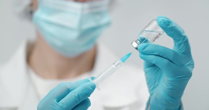 Medical worker in protective uniform filling syringe with transparent liquid, preparing vaccine