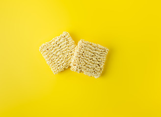 Two dry instant noodles blocks on vibrant yellow background. Flat layout