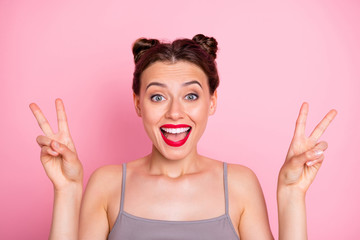 Hi party people. Photo of amazing youngster lady funny buns red lipstick showing v-sign symbol wear casual grey tank-top isolated pink color background