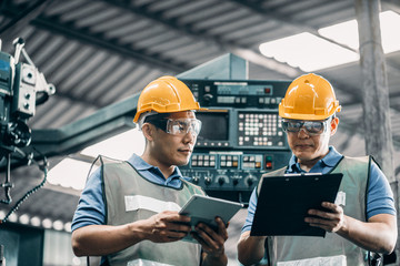 Engineer and manual worker analyzing process in industrial building. Young men foreman and her manual worker working on paperwork and steel in factory.