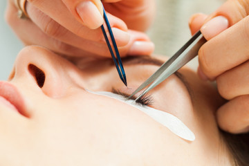 Stylist holding tweezers, tongs and making lengthening lashes for girl in a beauty salon