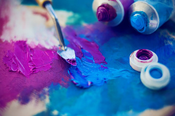 A metal palette knife mixes two bright colors on the palette, and next to them are open tubes of...