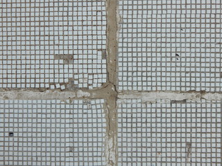 a fragment of an old street wall lined with small square mosaics in some places falling off with cracks on wide seams