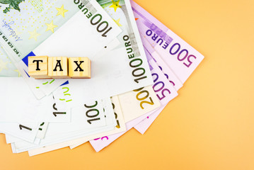 the word tax and the currency of the European Union of different denominations on an orange background 4