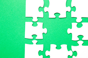 Fototapeta premium unfinished puzzle made of white cardboard on a green background and one unsuitable part from another puzzle, one piece is missing, copy space, search for some suitable part