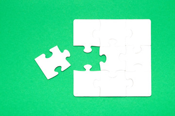 unfinished puzzle made of white cardboard on a green background and one unsuitable part from another puzzle, one piece is missing, copy space, search for some suitable part