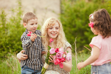 Little daughter and son congratulates mother and giving her flowers bouquet in spring garden