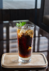 Long Island cocktail drink on a wooden tray and black background.