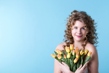 Portrait of a beautiful smiling caucasian woman with tulips in studio on a blue background.