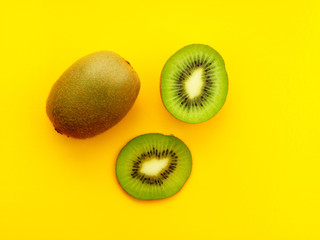 Kiwi cutaway on a yellow background. two halves and one whole kiwi.
