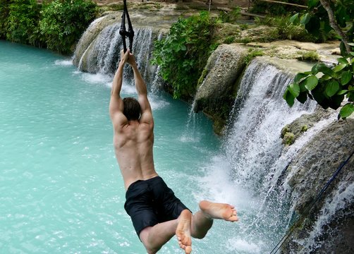 Man jumping from cliff into natural pool before waterfall , in air, cambugahay falls, Siquijor, Philippines