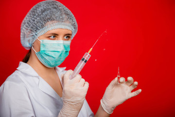 Close-up of a syringe with a stream of medicine from a needle in the hands of a female doctor on a red background.