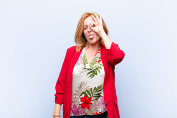 middle age woman smiling happily with funny face, joking and looking through peephole, spying on...