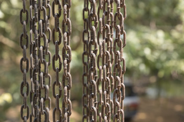 Vertical hanging rusty iron chains showing weathering covered with cobwebs.