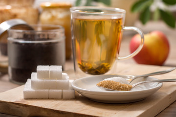 Parzenie zielonej herbaty szklance. Na pierwszym planie cukier biały, cukier trzcinowy i cukier w kostkach.