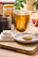 Parzenie zielonej herbaty szklance. Na pierwszym planie cukier biały, cukier trzcinowy i cukier w kostkach.