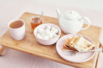 Fototapeta na wymiar Breakfast in bed in hotel room. Accommodation. Breakfast in bed with tea cup with pancakes on tray on bed background top view. Copy Space. Romantic valentine's day breakfast. Cozy breakfast Maslenitsa