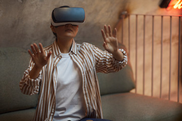 Waist up portrait of Asian woman wearing VR gear and gesturing while enjoying immersive experience in futuristic interior, copy space