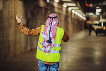 Rear view of angry arabian investor in vest, with headscarf having conversation with constructors while standing in building in construction process.