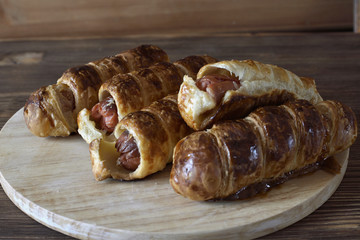 Sausages baked in dough on a wooden tray.