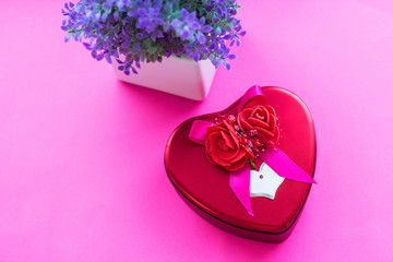Valentines day background. Red box in the shape of heart and purple flowers on dark pink background. Valentines day concept. Top view, copy space. Soft focus