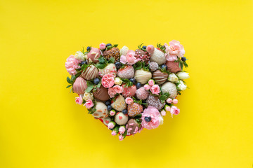 Heart shaped box with handmade chocolate covered strawberries with different toppings and flowers as a present on Valentines day on yellow background - obrazy, fototapety, plakaty