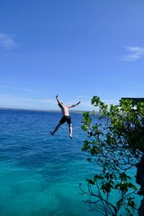 Man jumping from cliff into ocean, in air before blue sky, Siquijor, Philippines