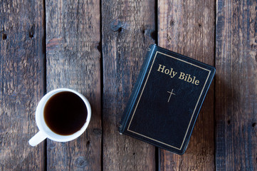 Black bible on a wooden table. White cup with tea or coffee. View from above
