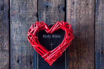 Red heart on a black bible. On a wooden background. View from above.