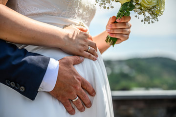 hands groom and bride with wedding rings and wedding bouquet flowers on pregnant belly baby love...