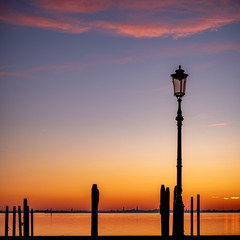 Silhouette of a streetlamp at sunset with the island of Venice in the background 