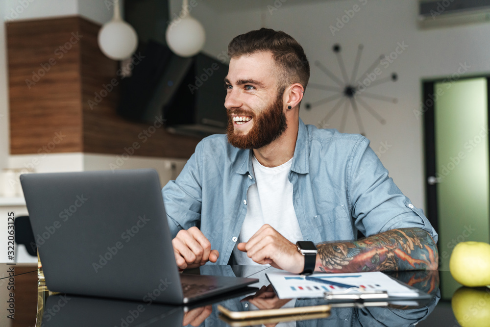 Poster Smiling young bearded man working on laptop computer