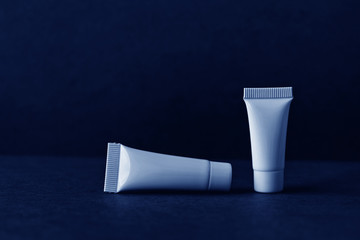 Blue cosmetic tubes on dark blue background. Blank opened plastic container, simple packaging design template. shallow depth of field, copy space photography.