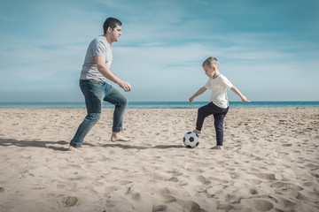 Fototapeta premium Father and son playing in football on sea coastline beach under