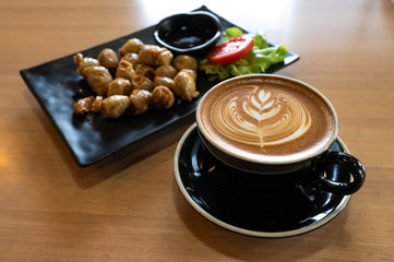 Latte art in black cup with snack on wooden table