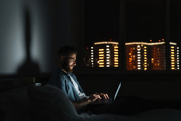 young bearded man laying on bed at home at night