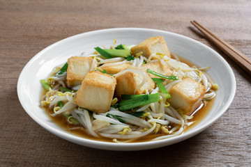 close up of stir fried fish tofu with bean sprout in a ceramic dish on wooden table. asian homemade style food concept.