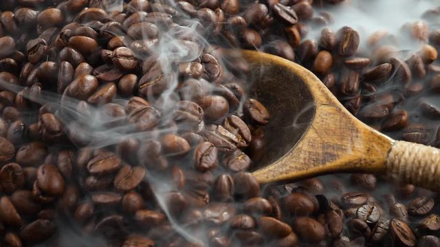 Coffee beans are fried in a pan and mixed with a spoon