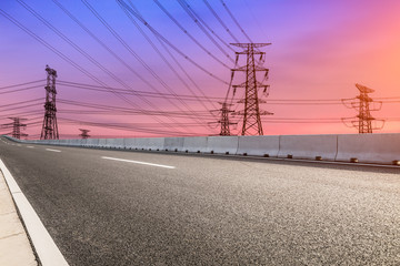 High voltage power tower and empty asphalt road at dusk