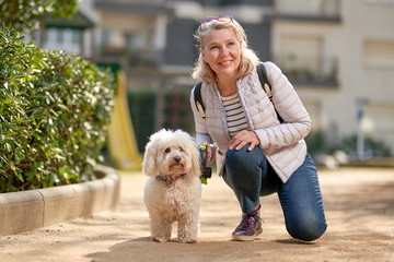 middle-aged blond woman walking with fluffy white dog in summer city