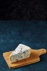 Blue cheese on a cutting board. Dark blue textured background
