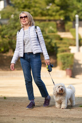 attractive middle-aged blond woman walking with dog in summer city