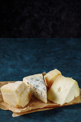 Different sorts of cheese on a parchment paper on dark blue textured background. Copy space for text